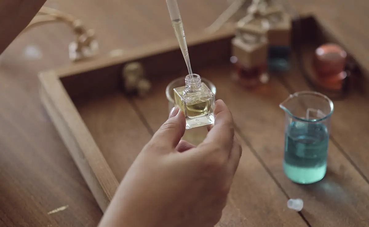 Closeup of a pipette with oil and a glass bottle woman pouring perfume in bottle Perfume creating workshop