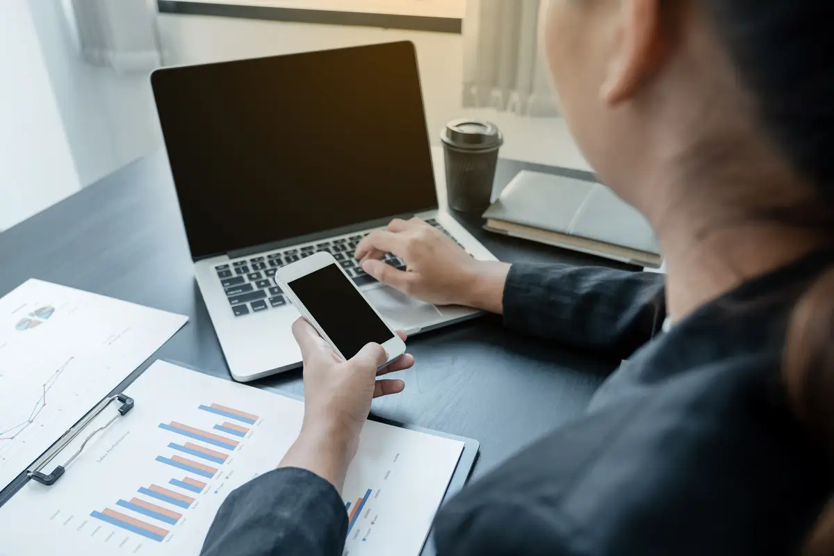 Midsection of businesswoman using smart phone and laptop on desk