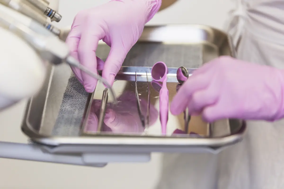 Dentist hand in pink gloves arranging dental tools on tray