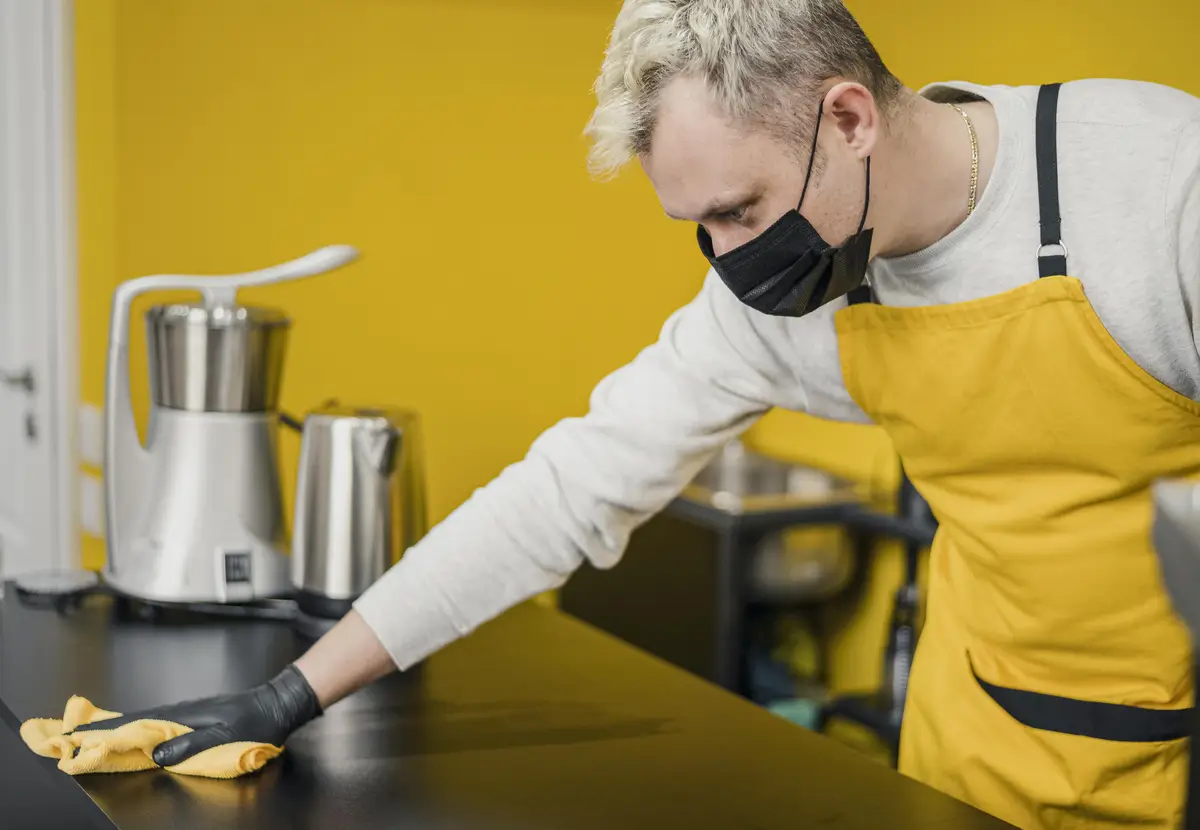 Side view of male barista with medical mask cleaning table surface