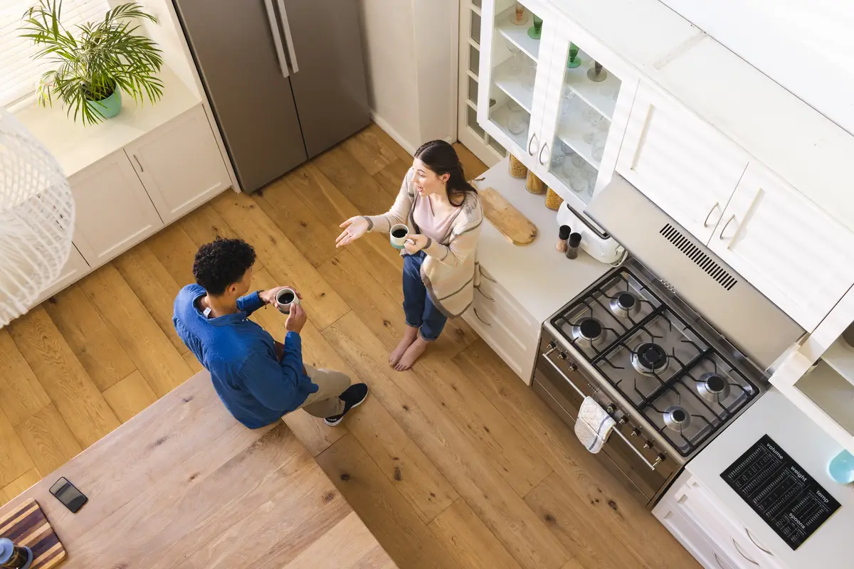 Happy diverse couple discussing and drinking tea in bright kitchen at home copy space