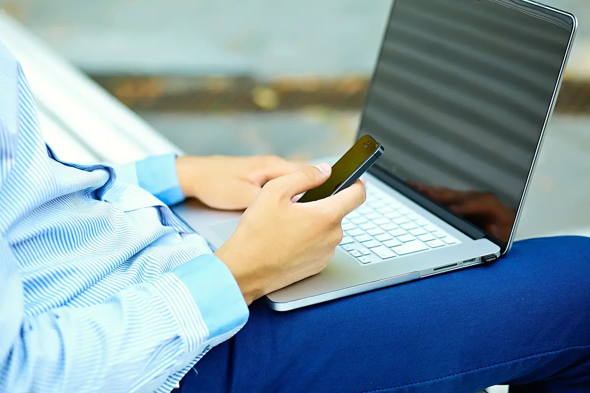 Young man working with laptop, man's hands on notebook computer, business person in casual clothes in the street
