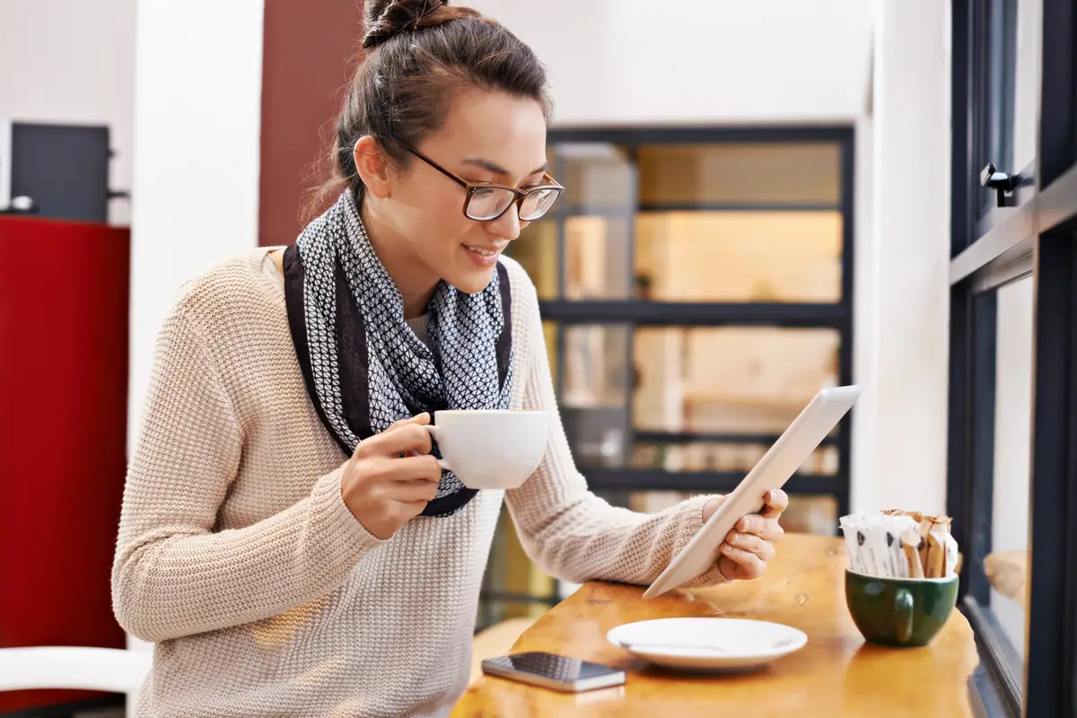Woman coffee shop and tablet with freelancer job and social media in cafe with cappuccino Website hot drink and internet with digital blog writer and technology at restaurant with tea and reading