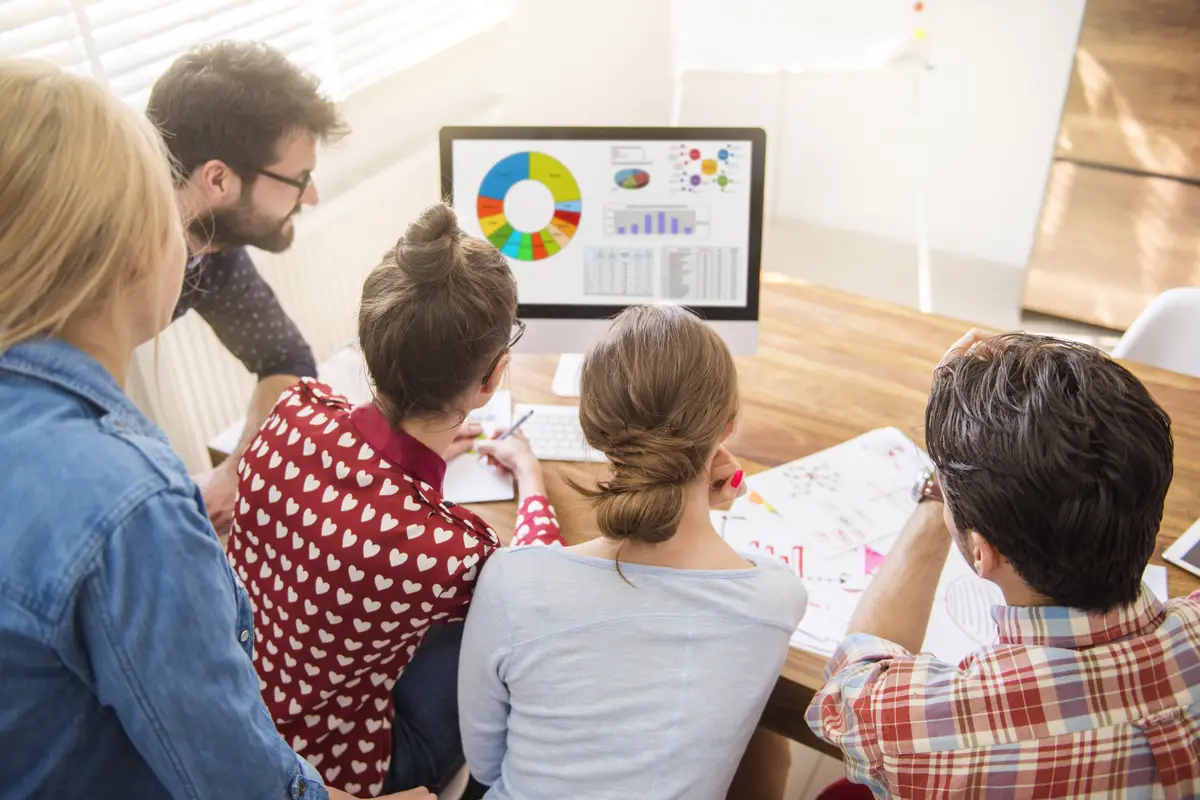 Equipe de cinco pessoas colaborando em torno de um computador que exibe gráficos de dados