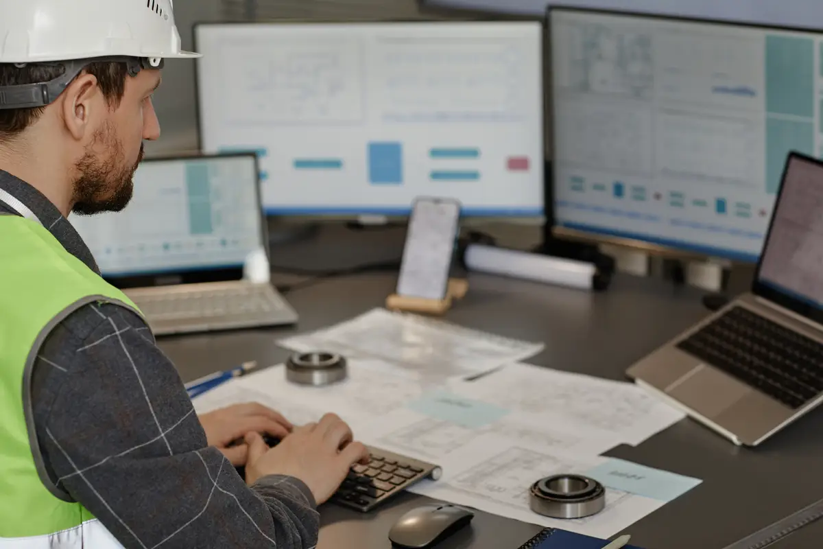 Side view of male engineer wearing hardhat at workplace in office and using computer designing blueprints copy space