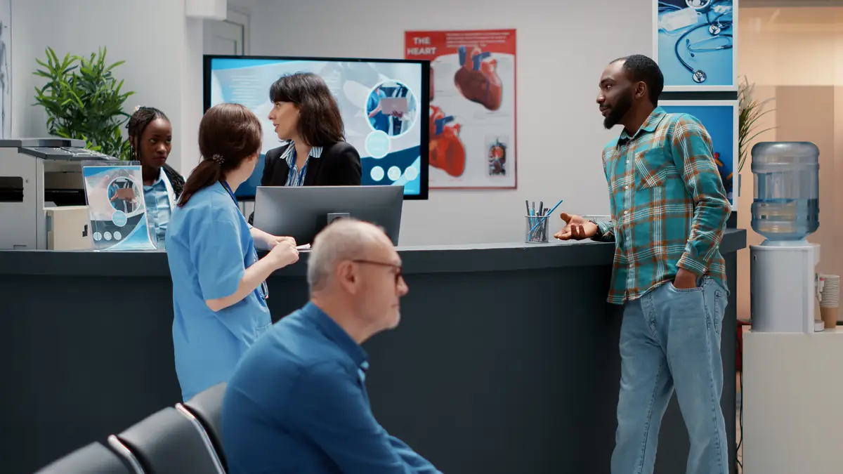 Multiethnic people chatting about medical system support, african american patient and hospital workers talking about checkup appointment. Waiting area lobby at healthcare facility.