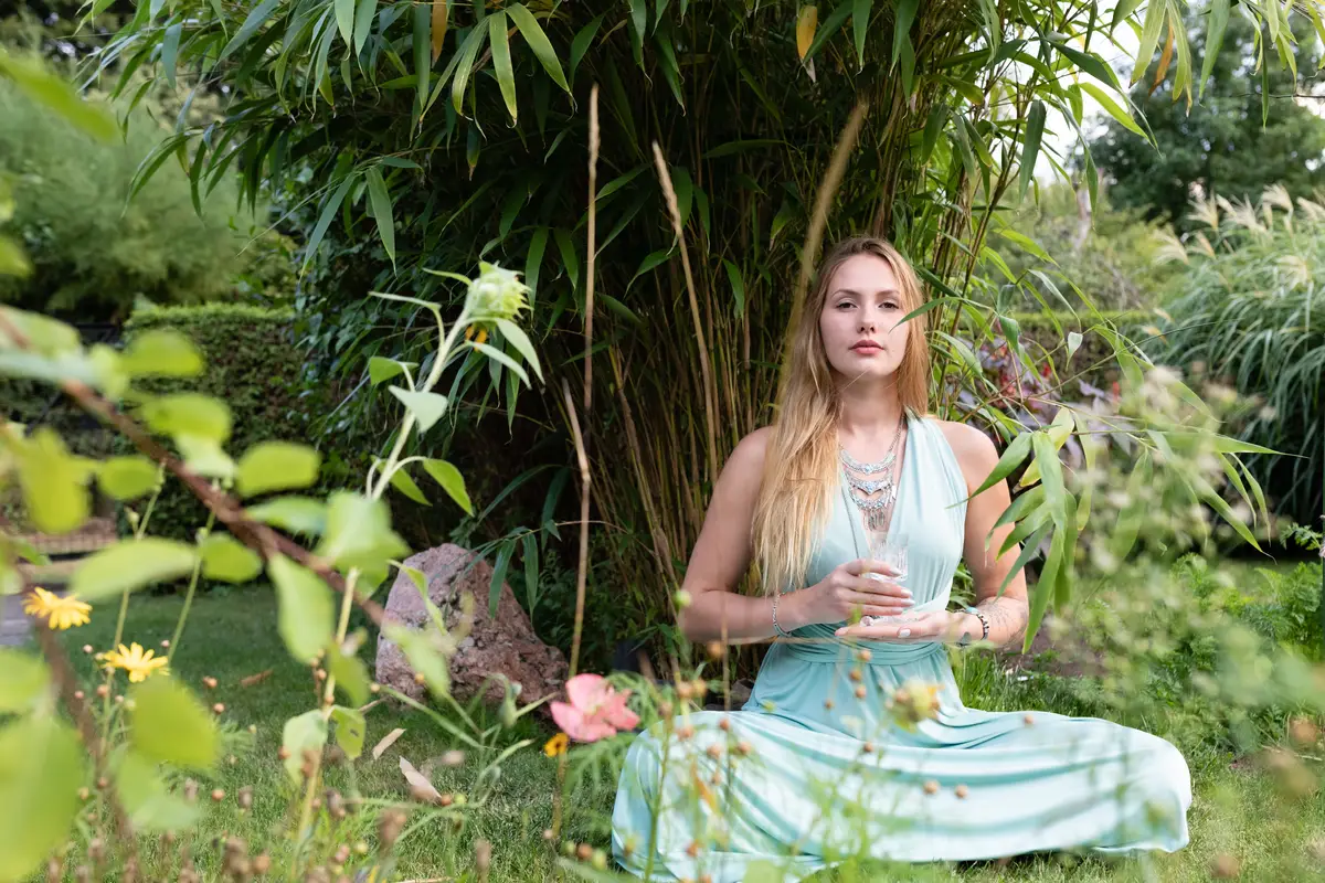 Portrait of young woman holding wineglass while sitting against plants