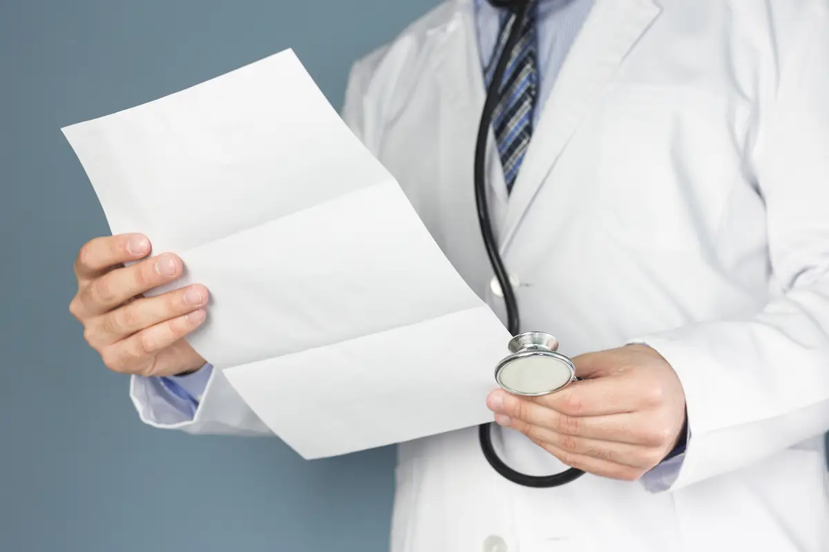 Close-up of doctor with stethoscope holding medical report in hand