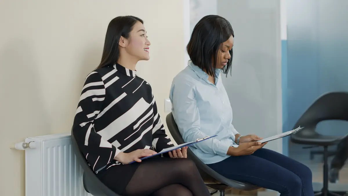 Asian and african american women talking in waiting lobby at job interview, preparing to join employment meeting with HR department. Female applicants having conversation about hiring.
