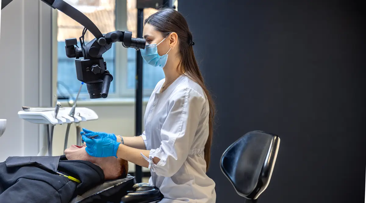Young female dentist treating patients teeth with dental microscope Dentistry concept