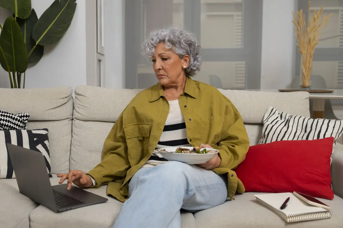 Senior woman eating figs dish at home and using laptop
