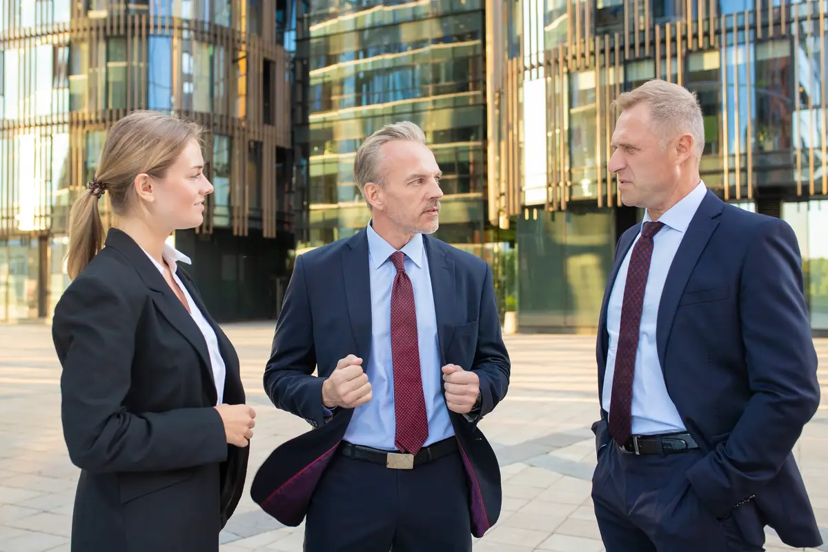 Serious confident business partners discussing project outdoors, standing and talking with city building in background. Partnership and communication concept