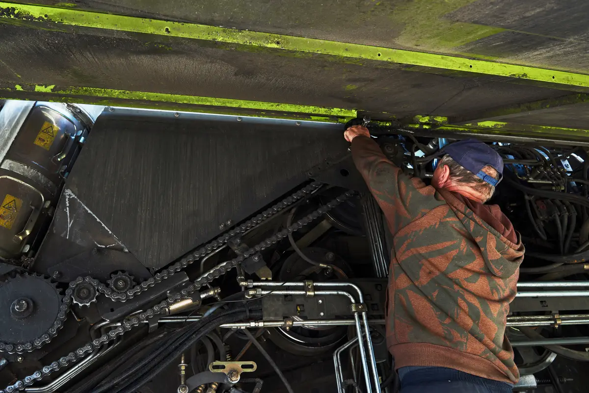 Combine machine service, mechanic repairing motor outdoors.