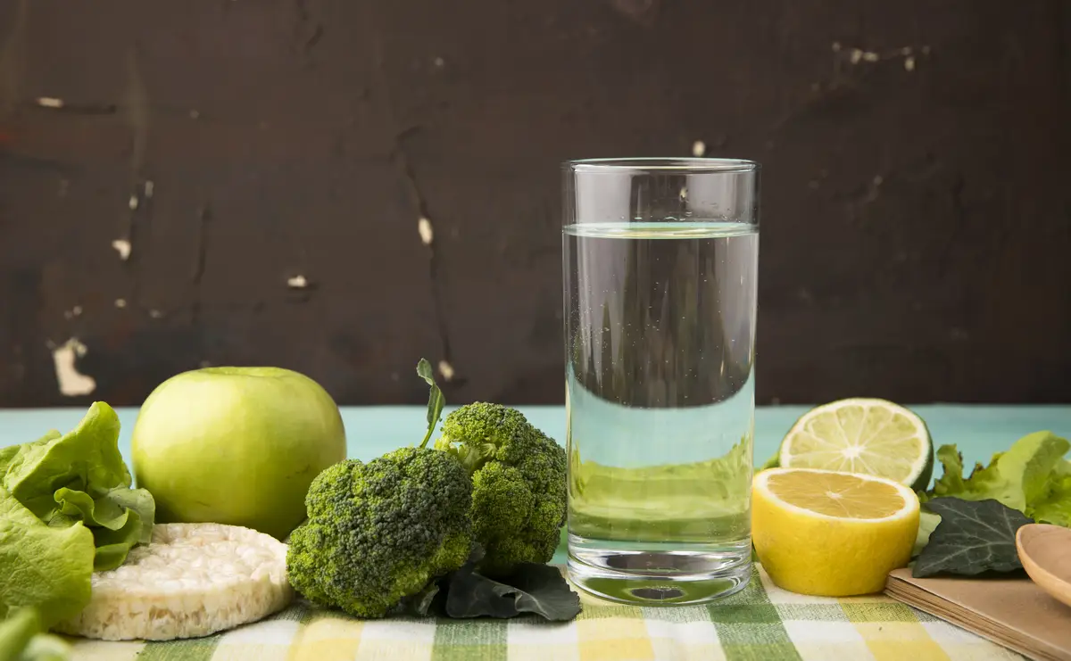 Side view green fruits and vegetables apple brocoli lettuce crunchy crispbread glass of water slice of lemon and lime