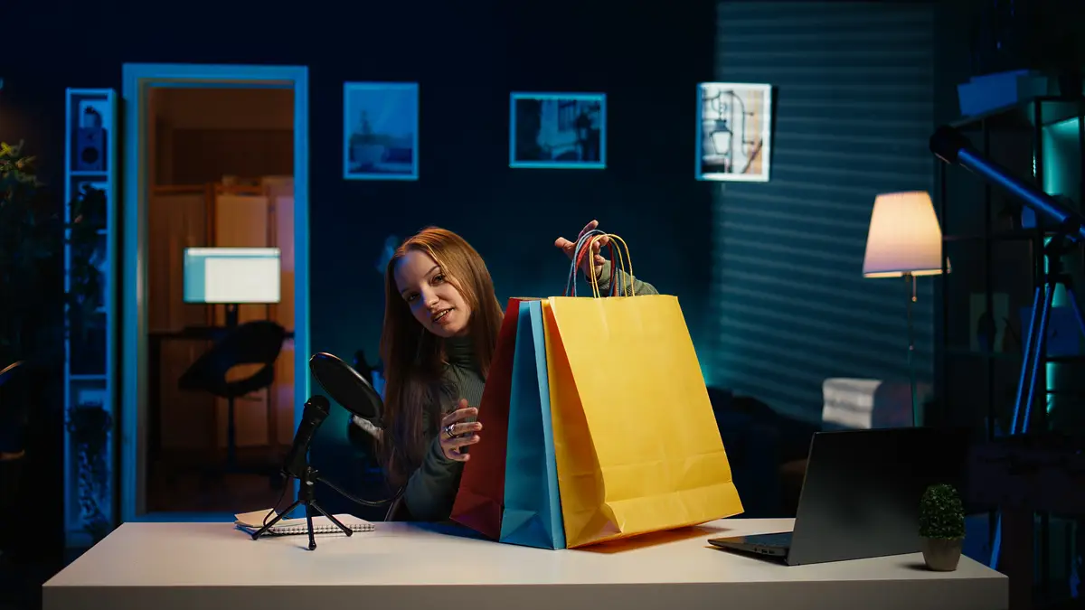 Girl holding colorful shopping bags in hand showing them to subscribers