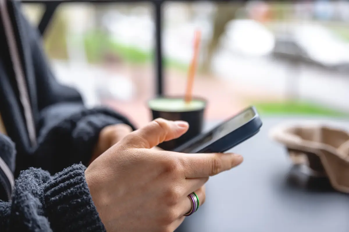 A woman sits on the terrace of a cafe and uses a smartphone closeup