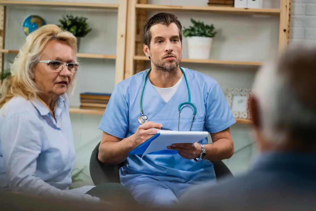 Home caregiver taking notes while communicating with senior patients about their medical condition during a home visit
