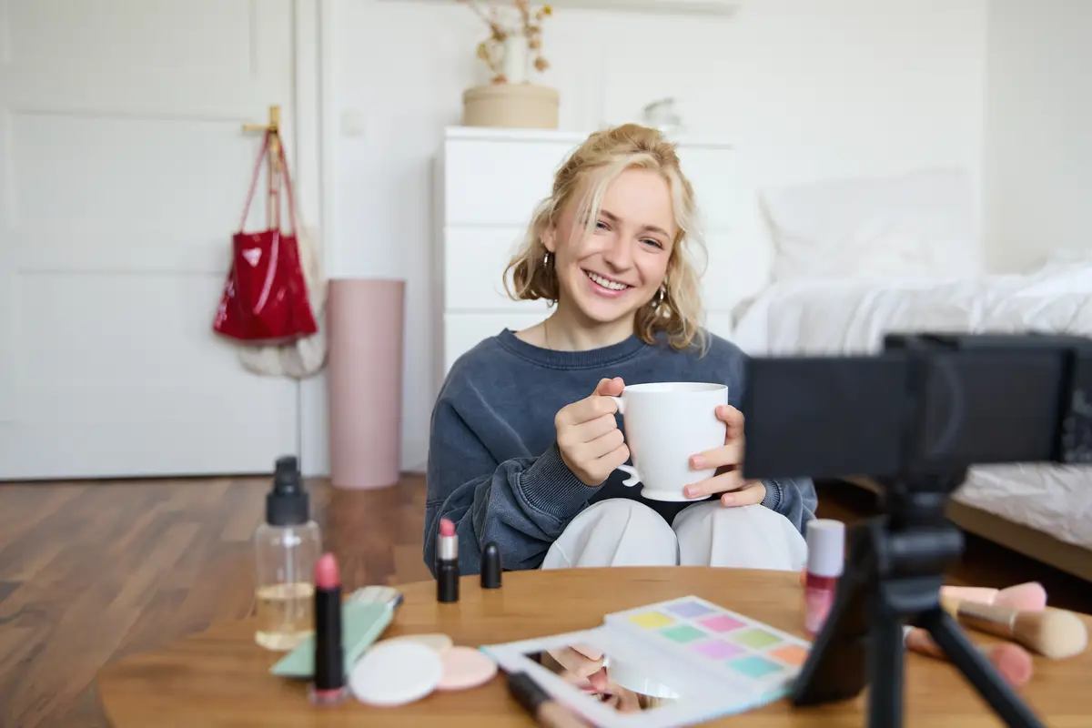 Portrait of smiling young woman girl records video on camera holds cup of tea talking doing