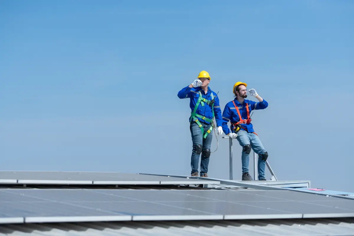 Both of technician repairing solar panels rest in the scorching sun on a factory roof covered