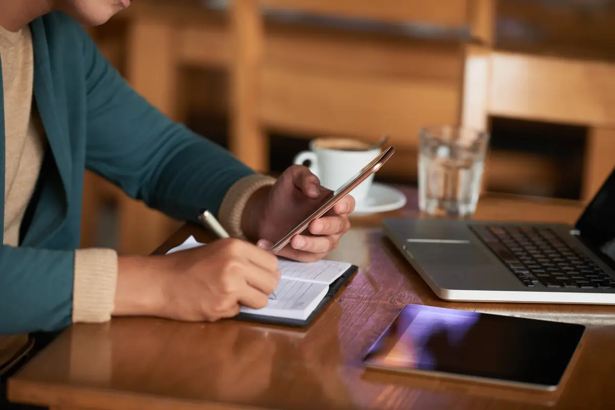 O que mudou na declaração do imposto de renda em 2026? 2 Hands of unrecognizable man sitting at table in cafe with gadgets and writing in notebook