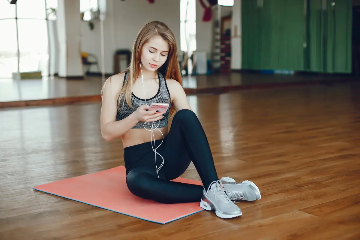 A beautiful and athletic sportswear girl sitting in the gym with phone