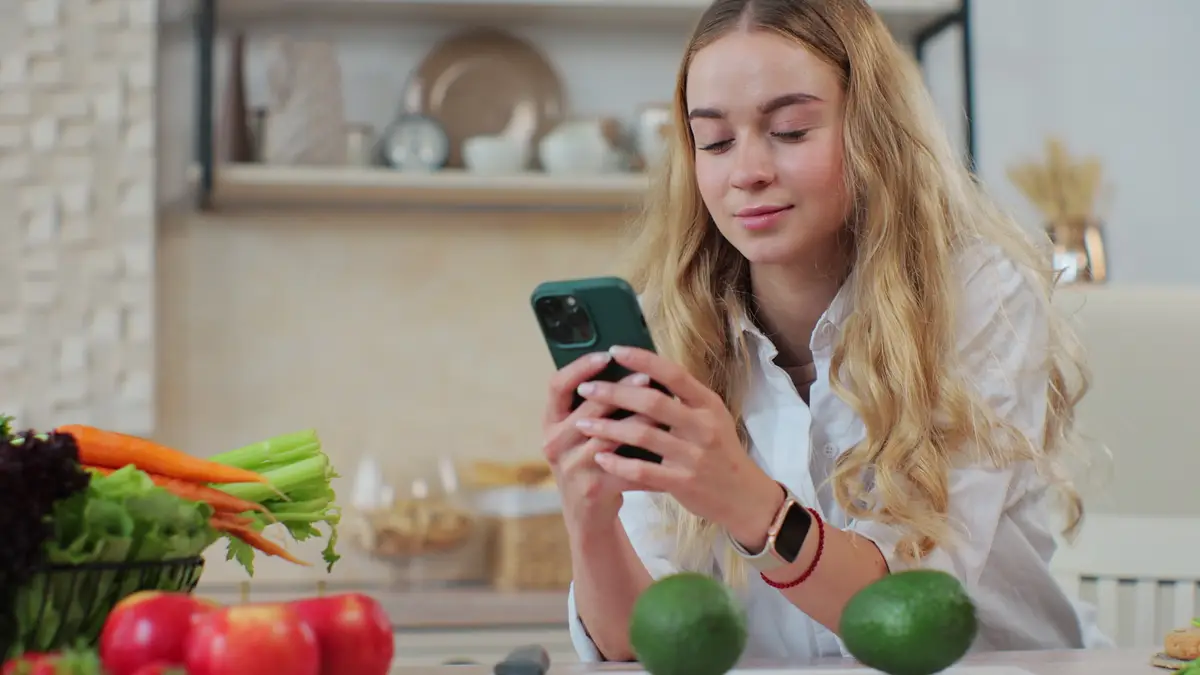 Young woman preparing salad searching online recipe in smartphone Preparing a fresh healthy vegan salad Mobile cookbook menu apps People Modern tech Cookery concept
