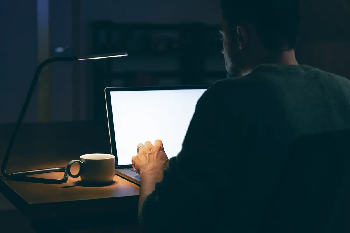 A man sits in a dark room in front of a blank laptop screen