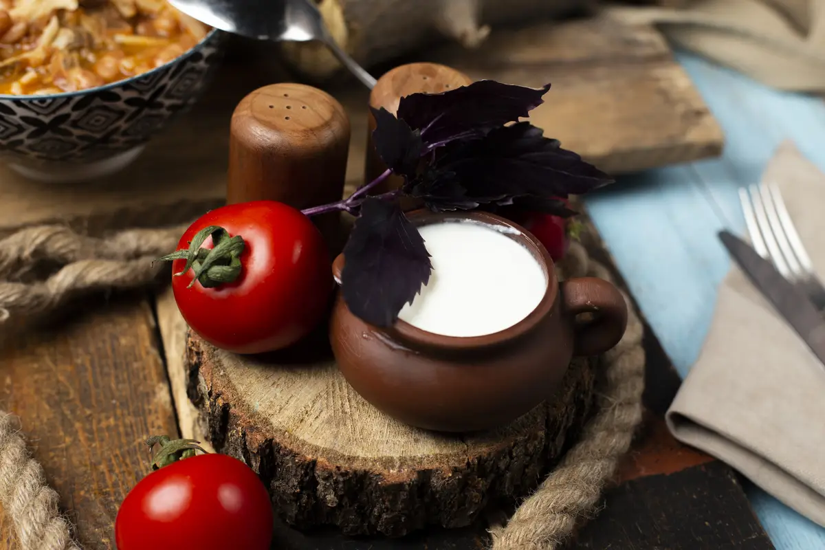 Fresh tomatoes, basilic and a pot of yogurt on the wooden board.