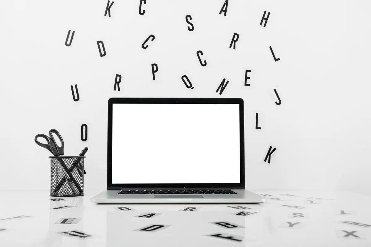 Laptop with blank white screen near pencil holder and alphabets on white surface