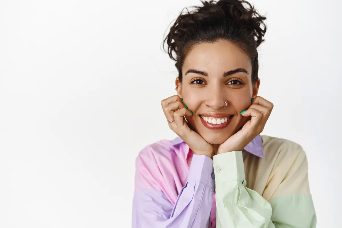 Close up face portrait of smiling happy woman hold hands on face looking at camera with satisfied cheerful face watch something interesting white background