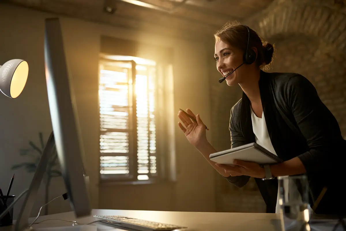 Young happy businesswoman waving to someone while having video call over a computer in the office