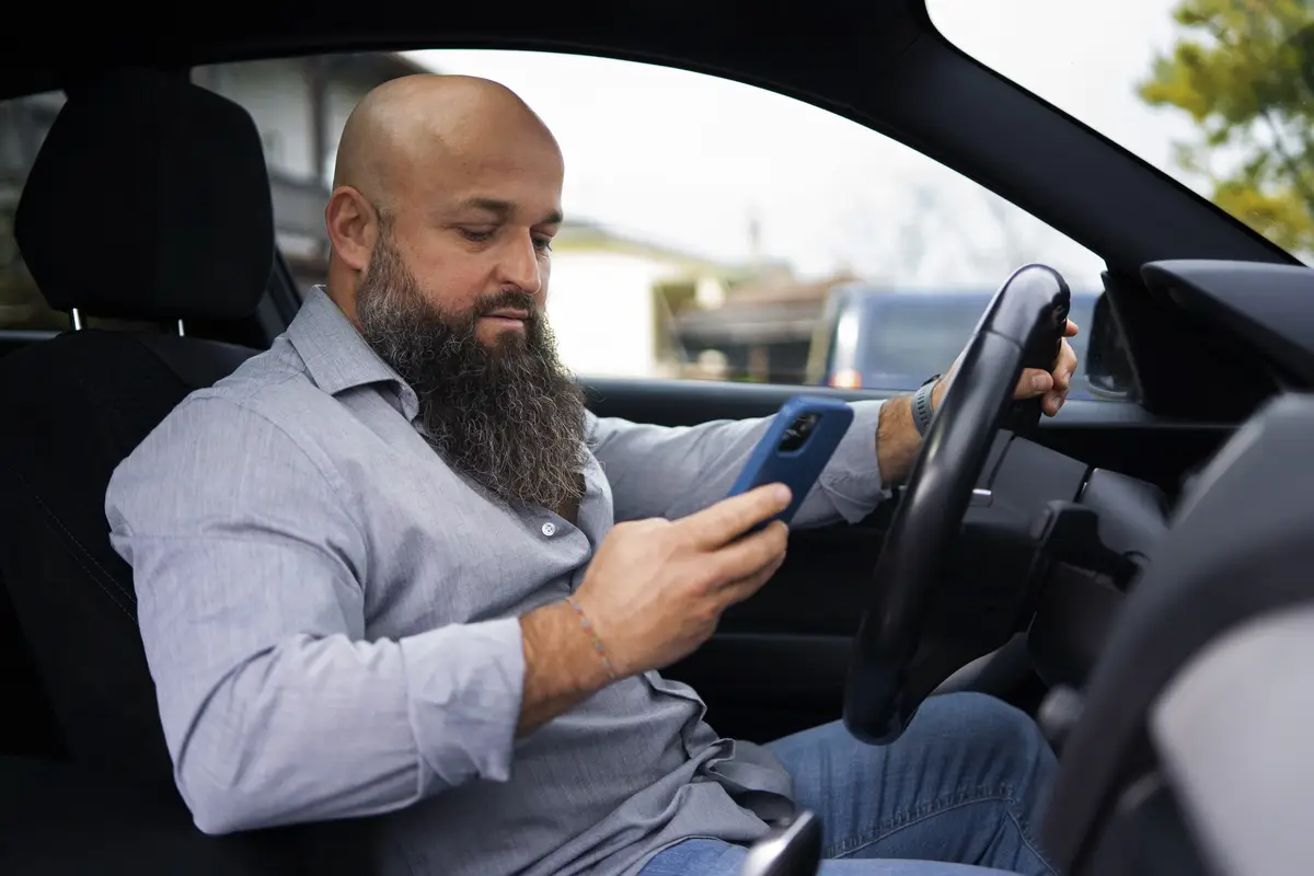 Side view man holding smartphone in car
