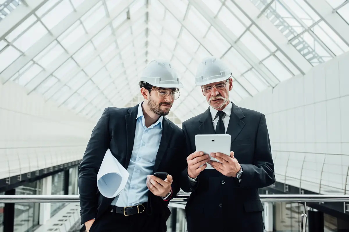 Two successful entrepreneur in helmet with project and laptop of new buildings stay near glass roof