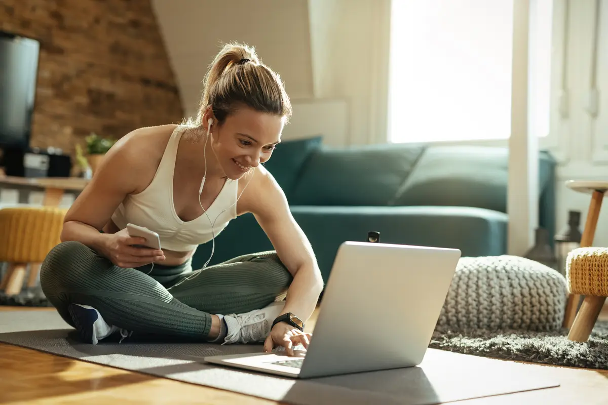 Young happy sportswoman relaxing on the floor and using laptop at home.