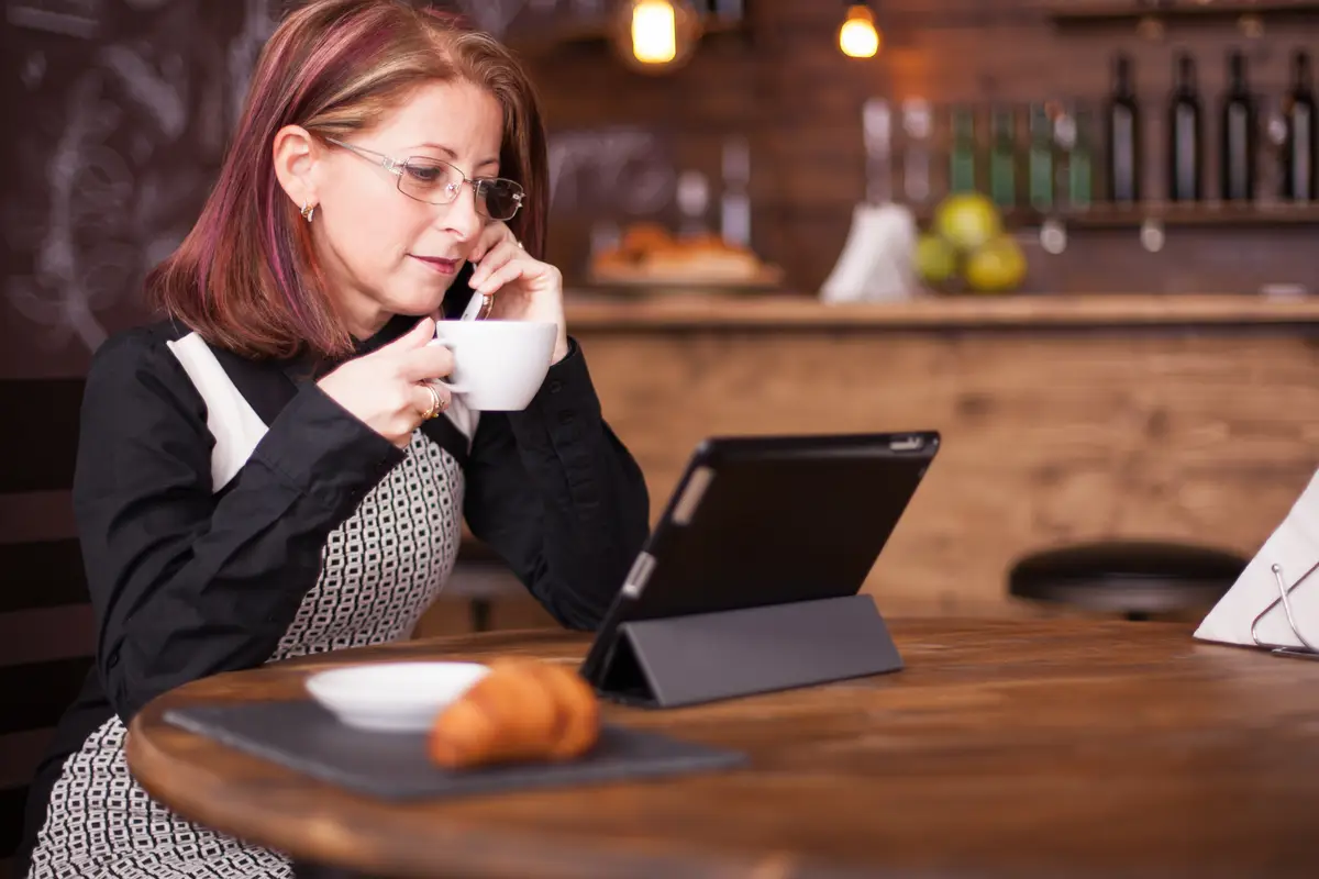 Businesswoman looking at tablet while talking having a conversation on her phone. Working in vintage coffee shop