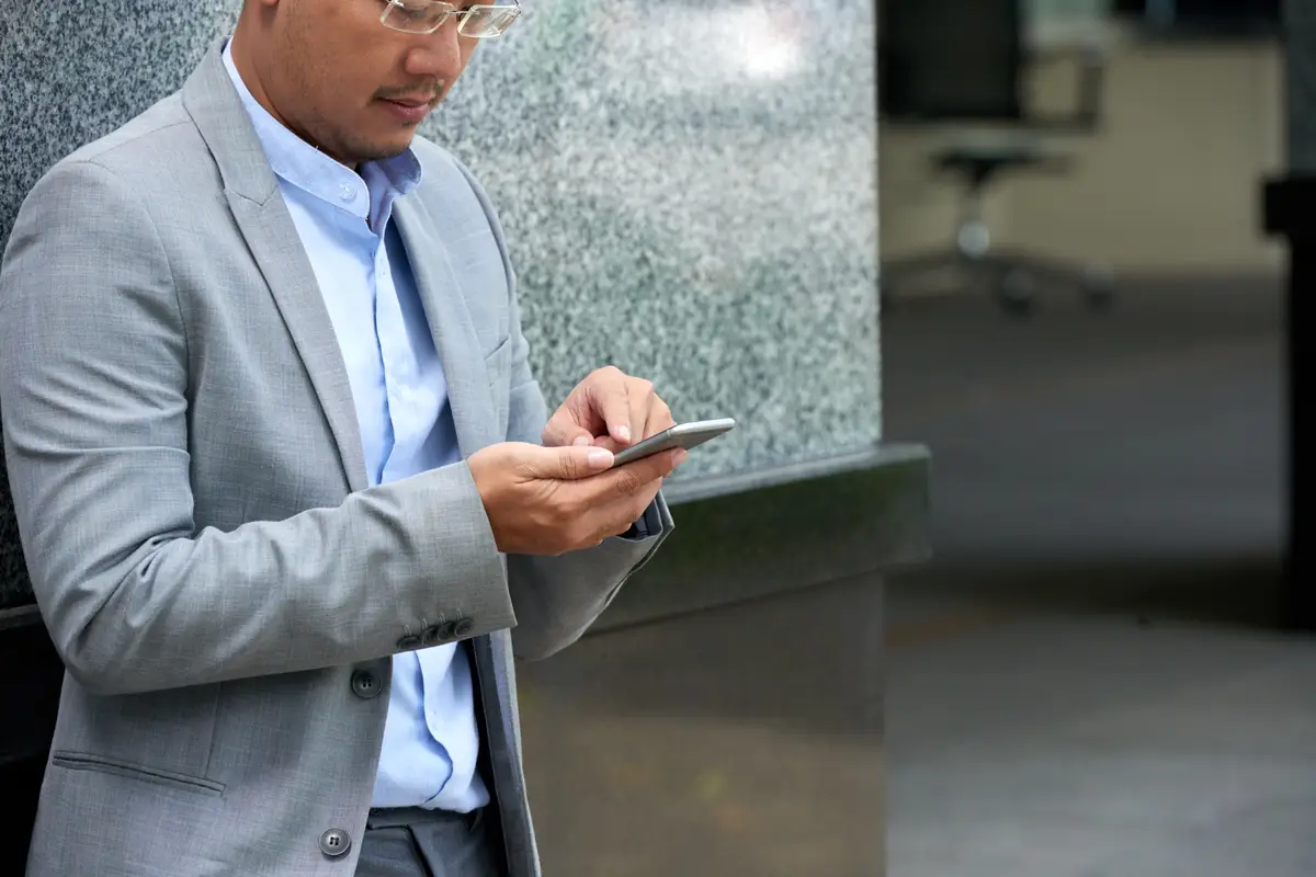 Cropped man reading text message on his smartphone standing at the office building