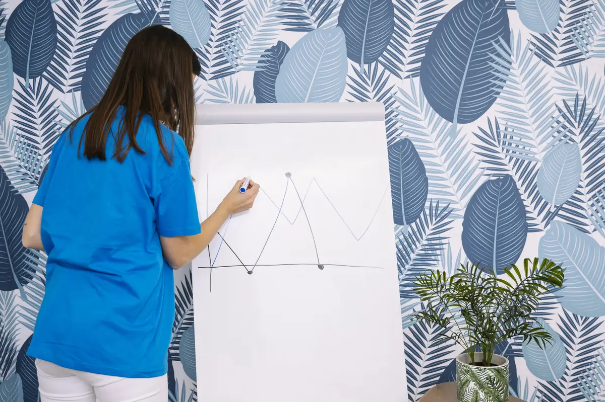 Woman in blue t-shirt drawing graph with marker on flipchart against wallpaper