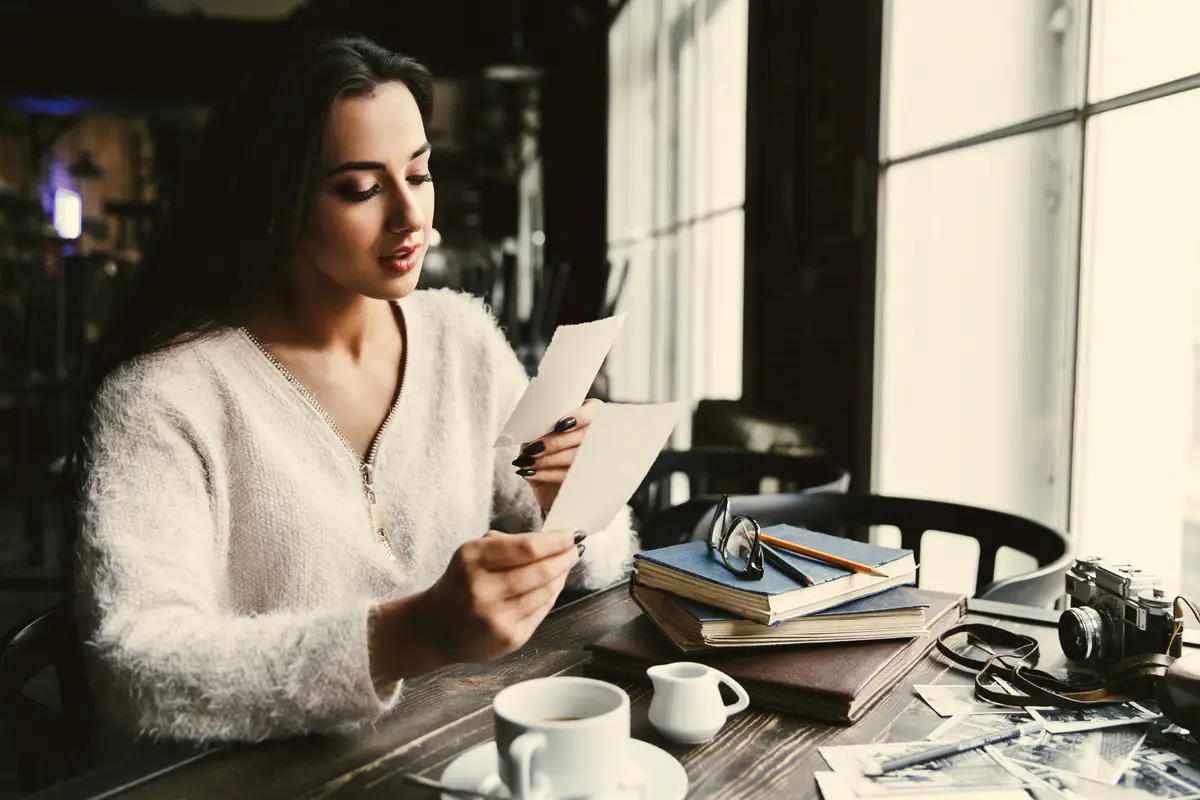 Pretty lady looks at old photos sitting at the table in cafe