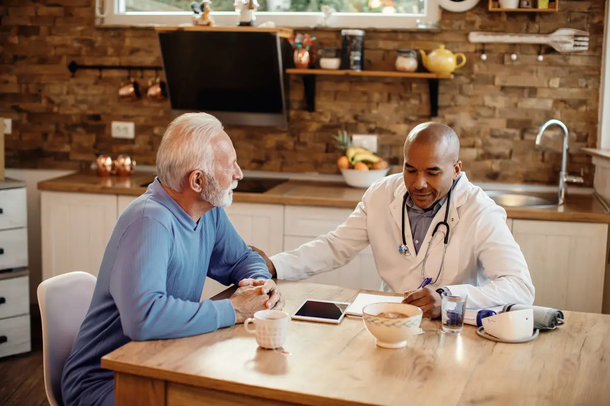 Happy African American doctor in a visit at senior man's home