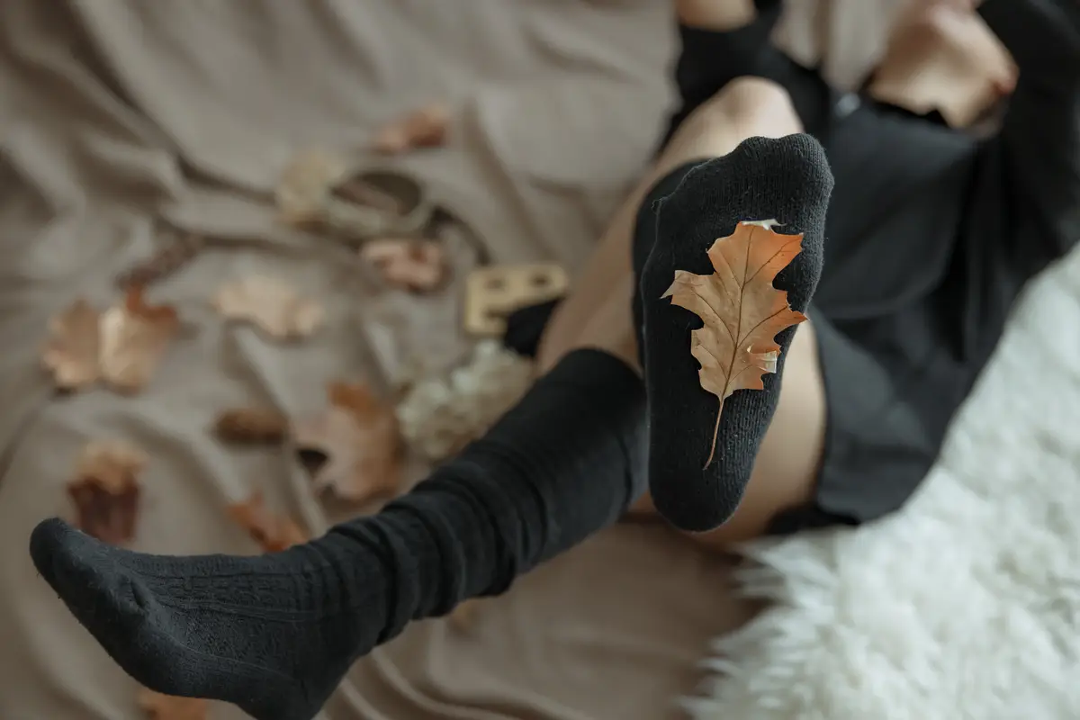 A woman in warm stockings on a blurred background and an autumn leaf in focus.