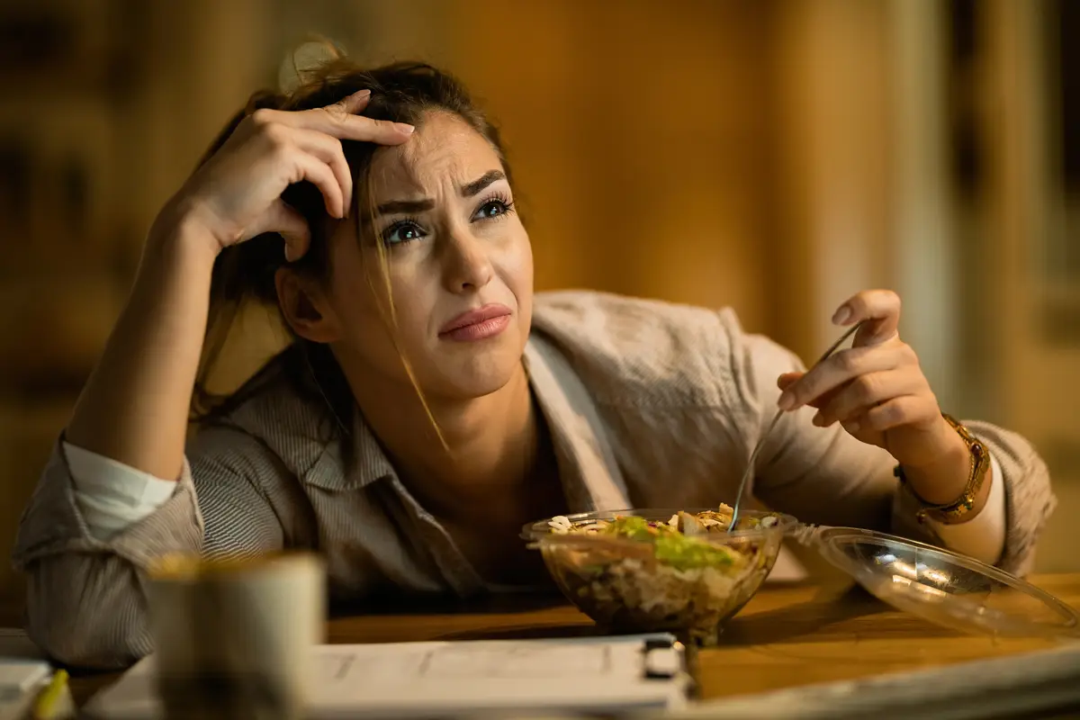 Displeased woman feeling confused while reading an email on a computer and eating salad at night