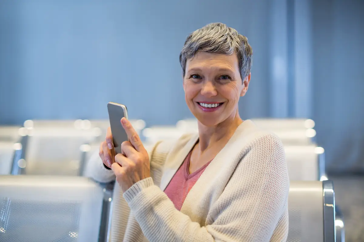 Smiling woman sitting with mobile phone in waiting area