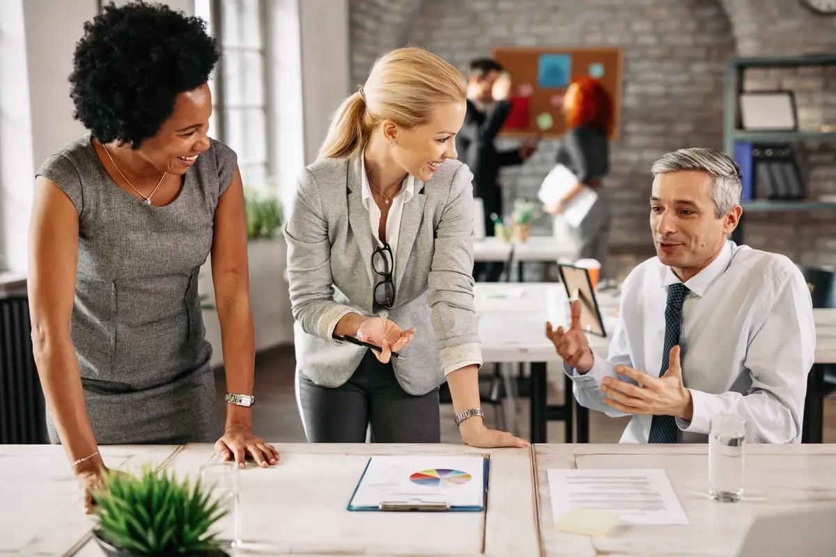 Group of smiling business people analyzing reports and communicating while working together in the office There are people in the background