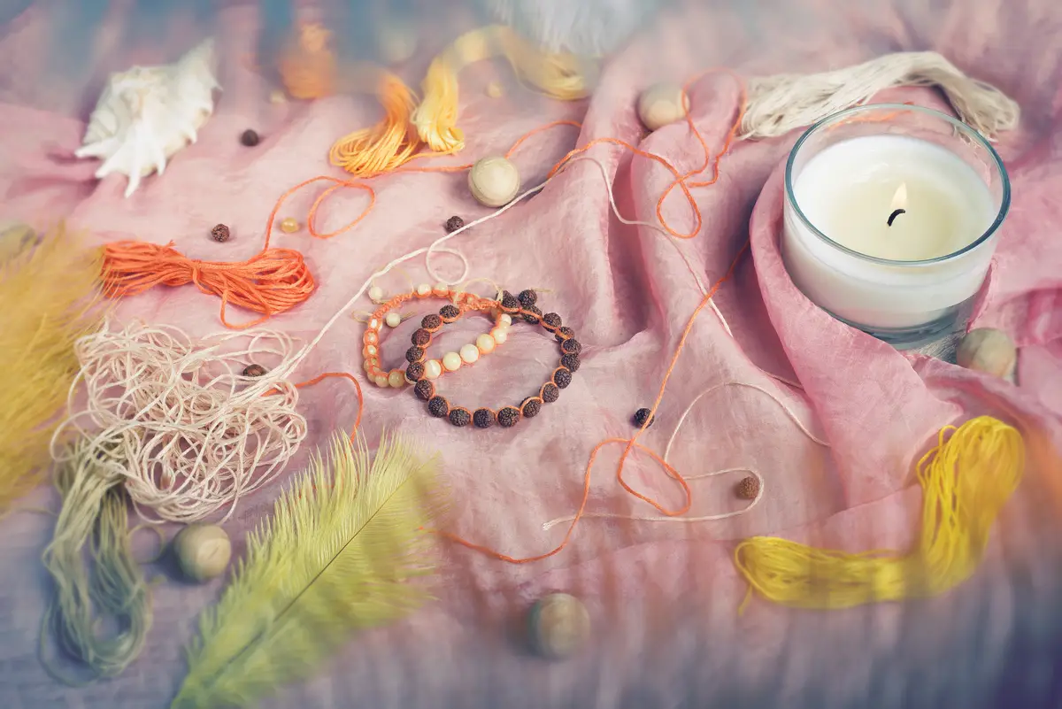 Two handmade shamballa bracelets made of rudraksha  amber beads  with threads feathers and a candle