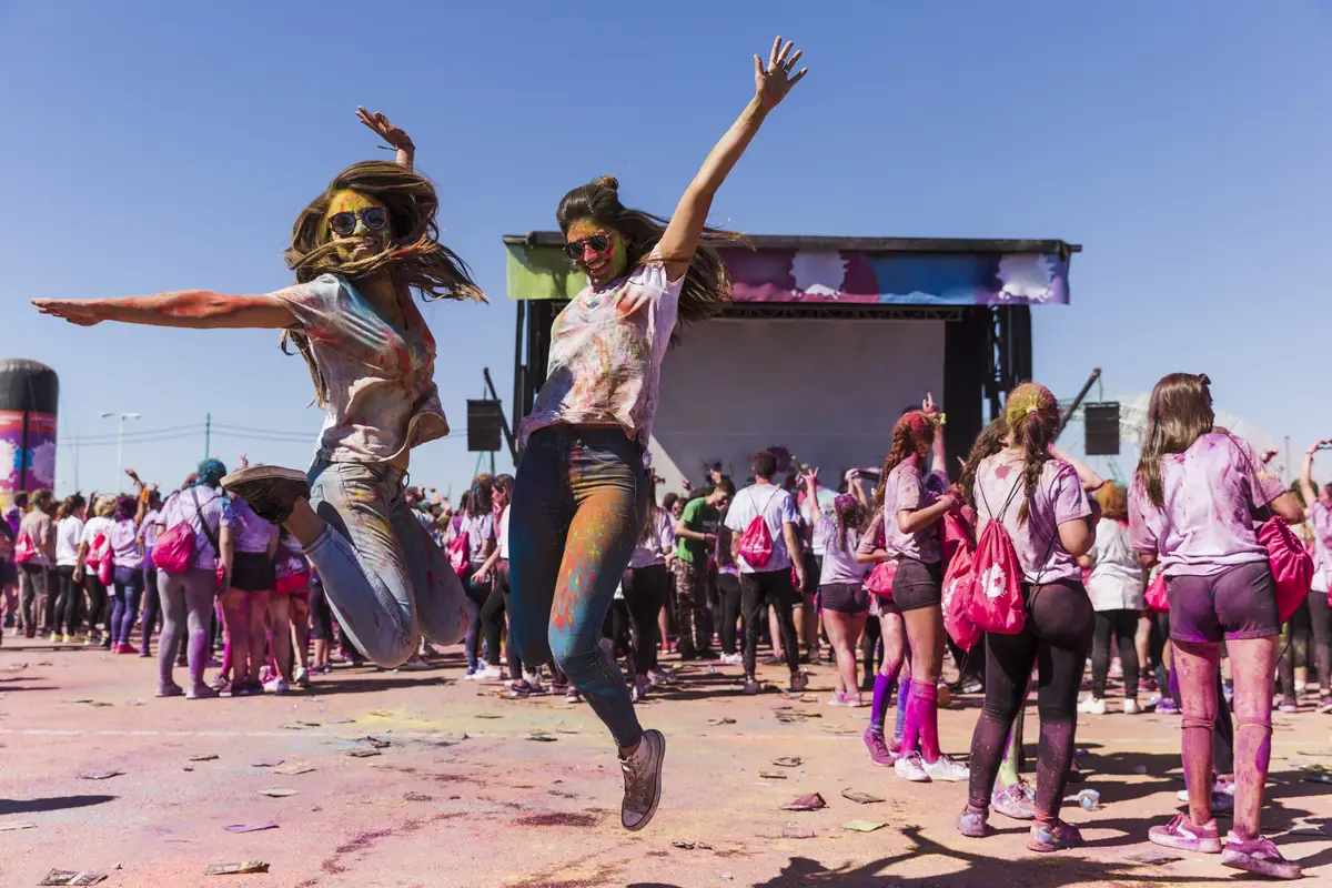 Excited young women jumping in air celebrating the holi festival