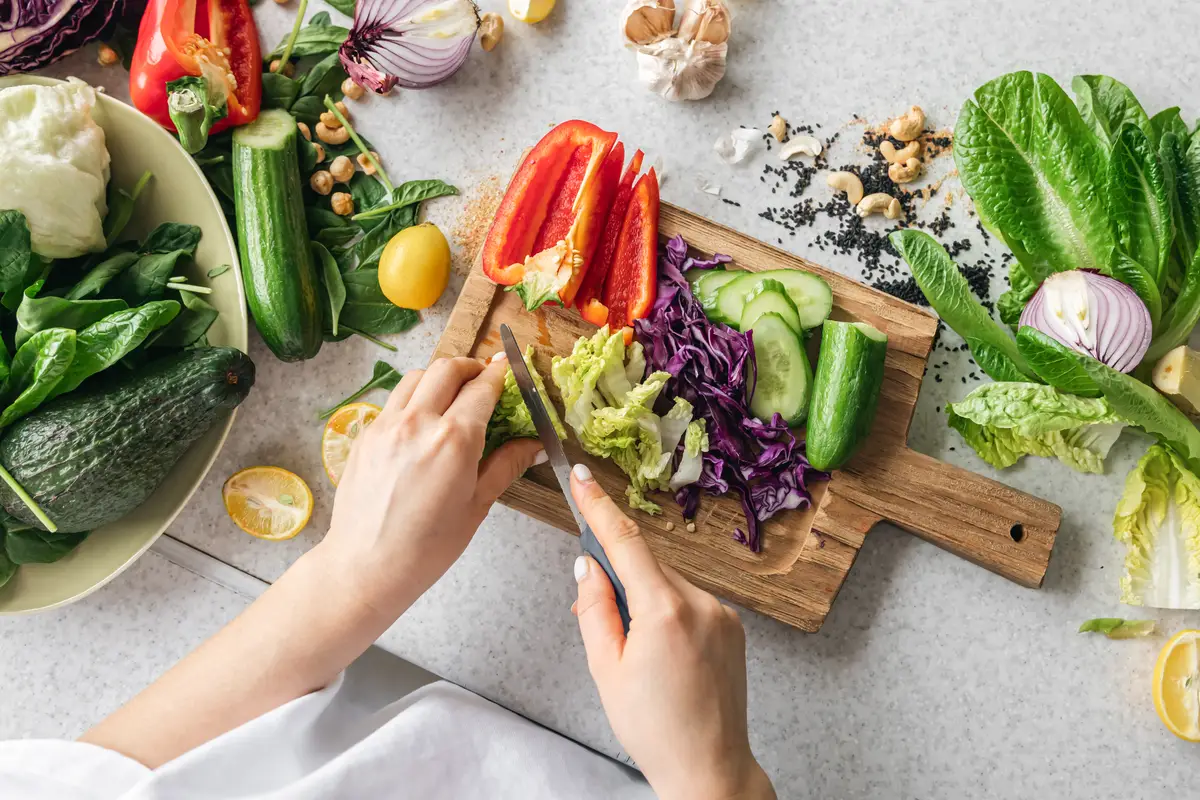 Top view woman cutting fresh vegetables on a wooden kitchen board
