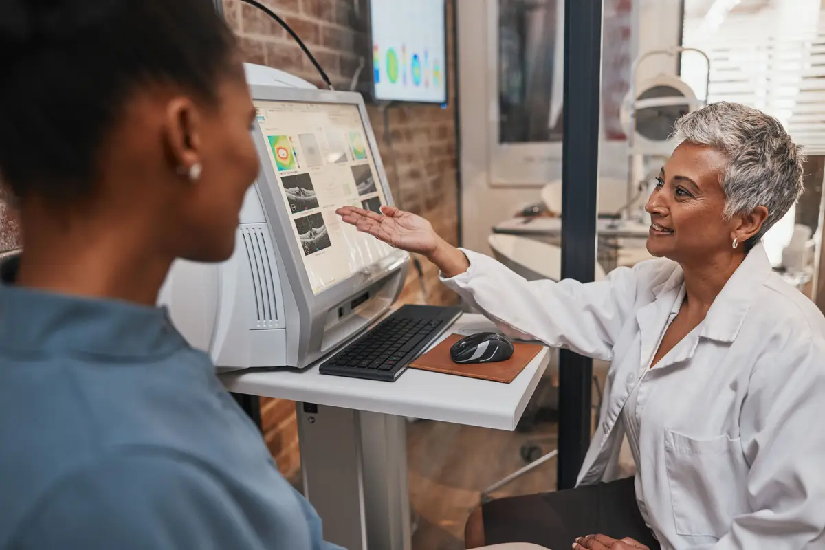 Elderly ophthalmologist woman computer and eye exam results with consultation advice and smile Optometrist doctor and happy with African patient for analysis consulting or medical help in office