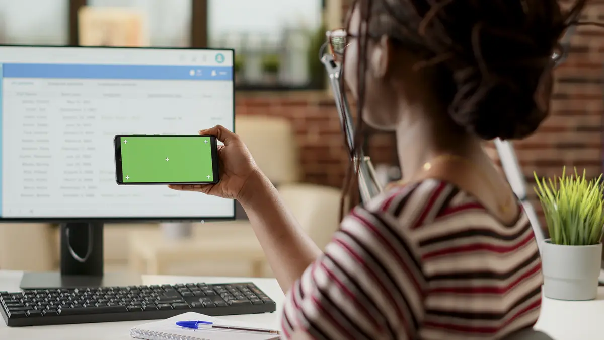 Businesswoman using horizontal greenscreen on smartphone, sitting at desk. Freelancer looking at blank mockup background with isolated copyspace and chroma key template on telephone display.
