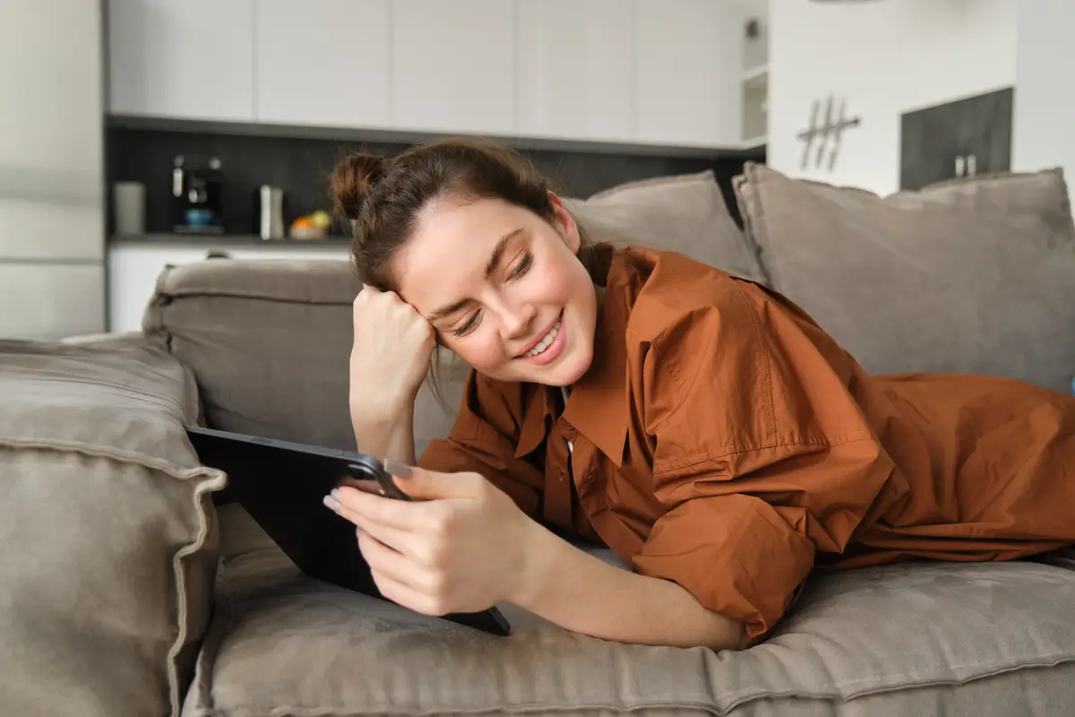 Portrait of beautiful young woman resting at home on couch lying on sofa with digital tablet reading