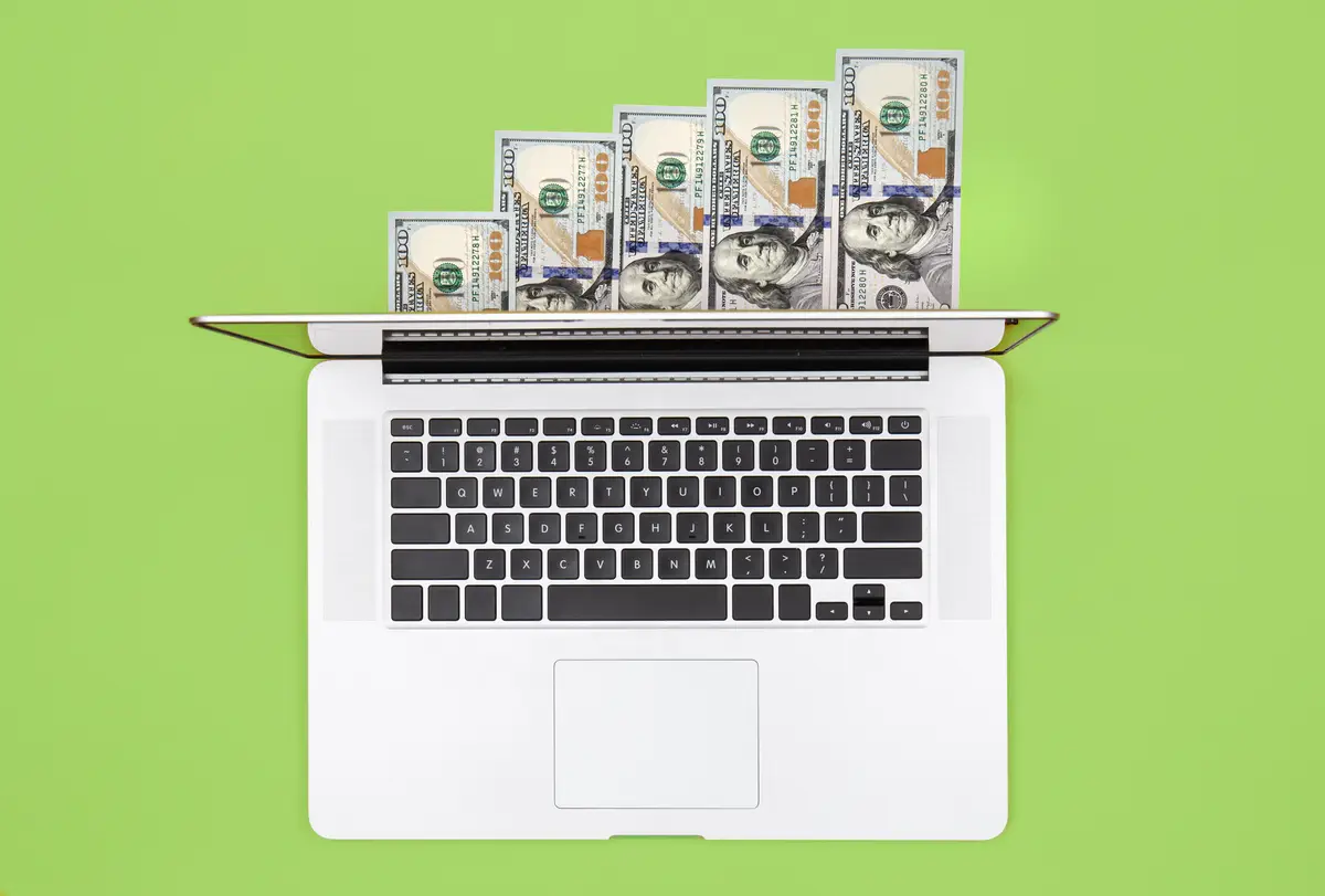 Laptop and dollar bills on color background flat lay